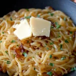 A bowl of creamy caramelized onion pasta garnished with Parmesan cheese and fresh herbs.