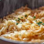 A bowl of caramelized onion pasta garnished with herbs